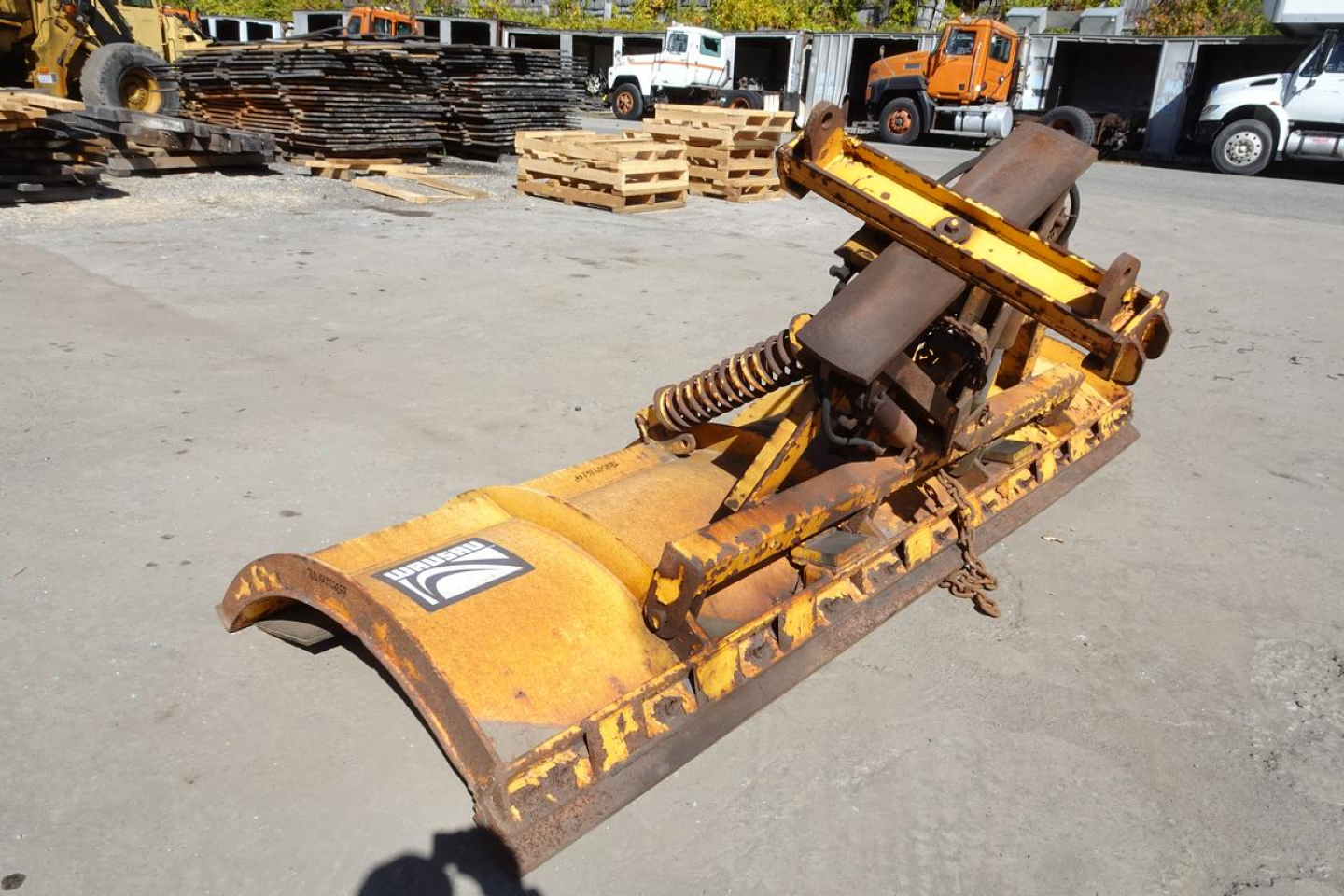 Mack Granite GU712 front loader bucket attachment showing hydraulic cylinders and rusted metal with warning label.