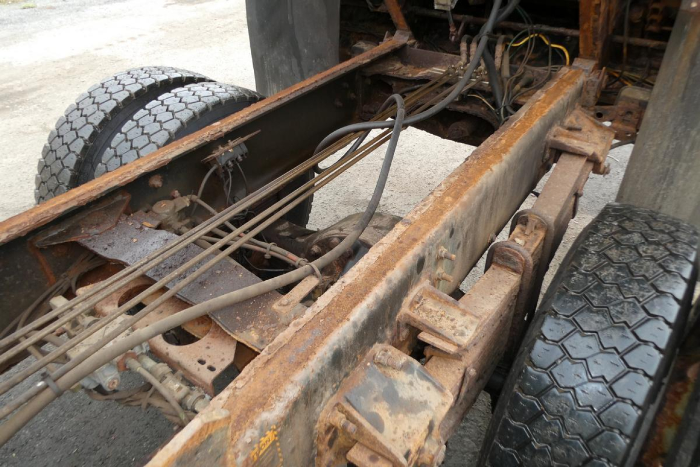 Chassis and suspension view of a used 2010 Mack GU dump truck frame with rusty steel beams, springs, and dual rear wheels visible.