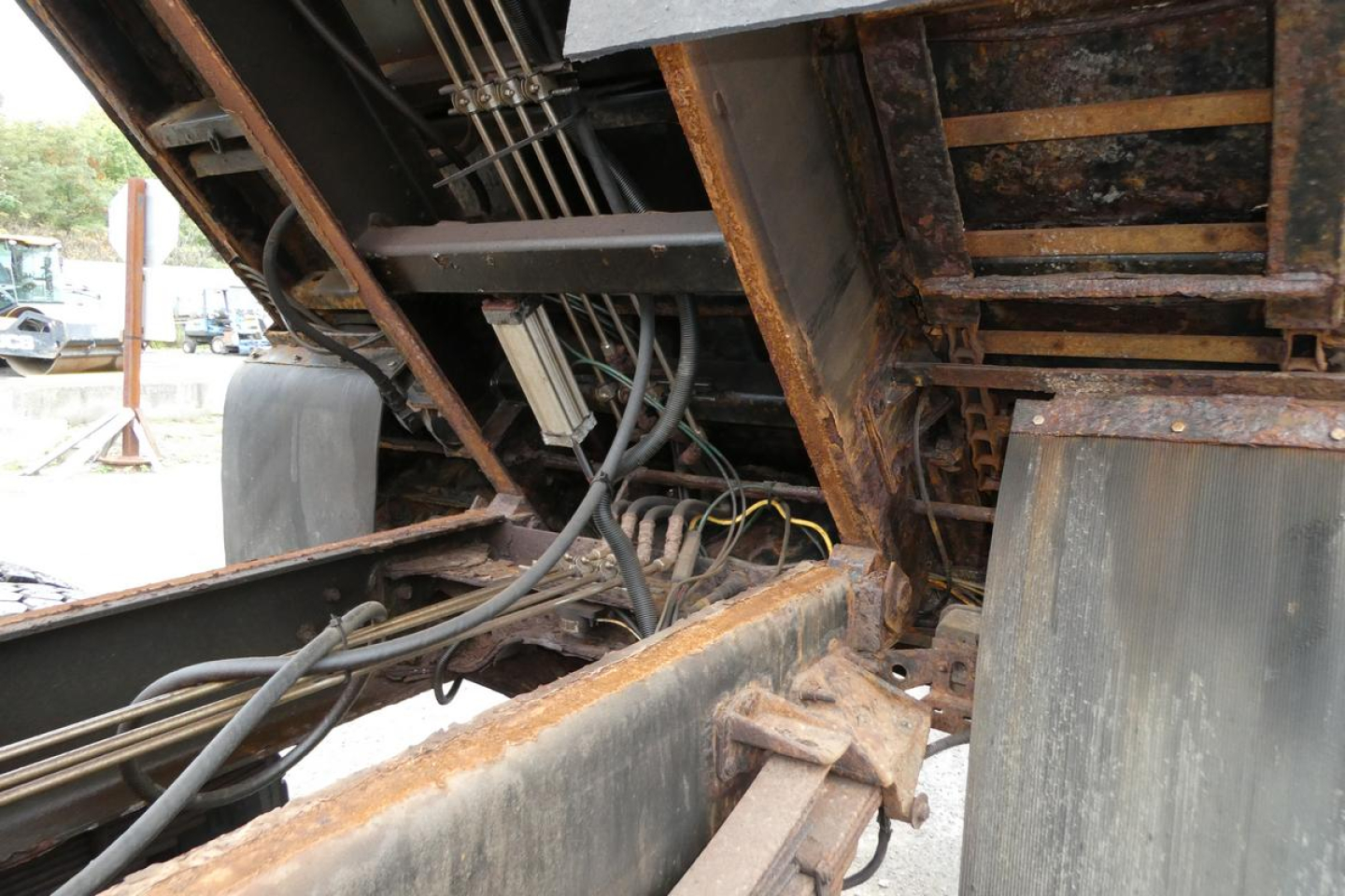 Truck undercarriage showing hydraulic lines and frame rails with rust and wiring harness in a Mack GU dump truck.