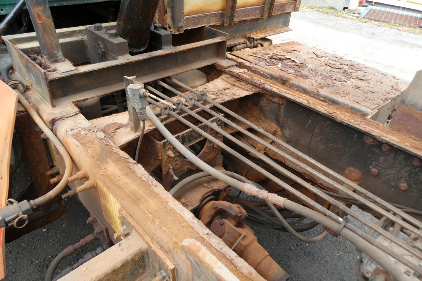 Dump truck chassis showing exposed frame rails, hydraulic hoses, and rusty metal components in the bed area.
