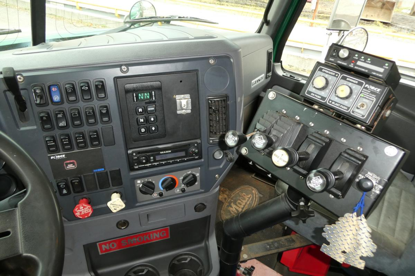 Dashboard and instrument cluster of a Mack GU dump truck cab showing switches, gauges, and control panel with a NO SMOKING sign.