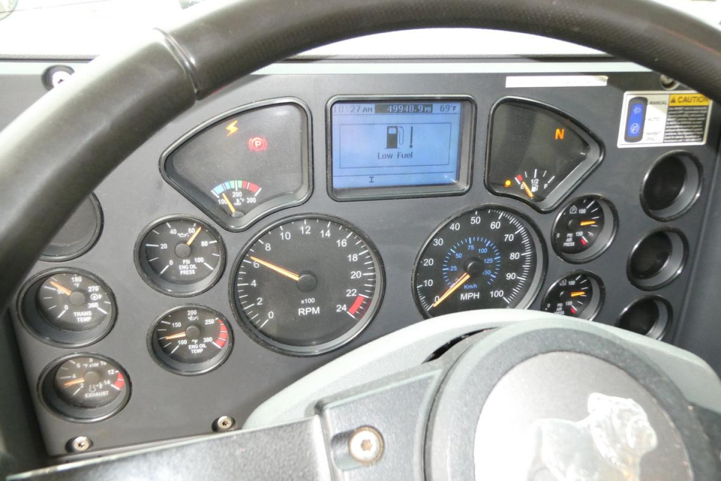 Dashboard of a Mack GU truck showing multiple gauges, digital display reading Low Fuel, speedometer up to 120, RPM gauge, and various indicator lights.