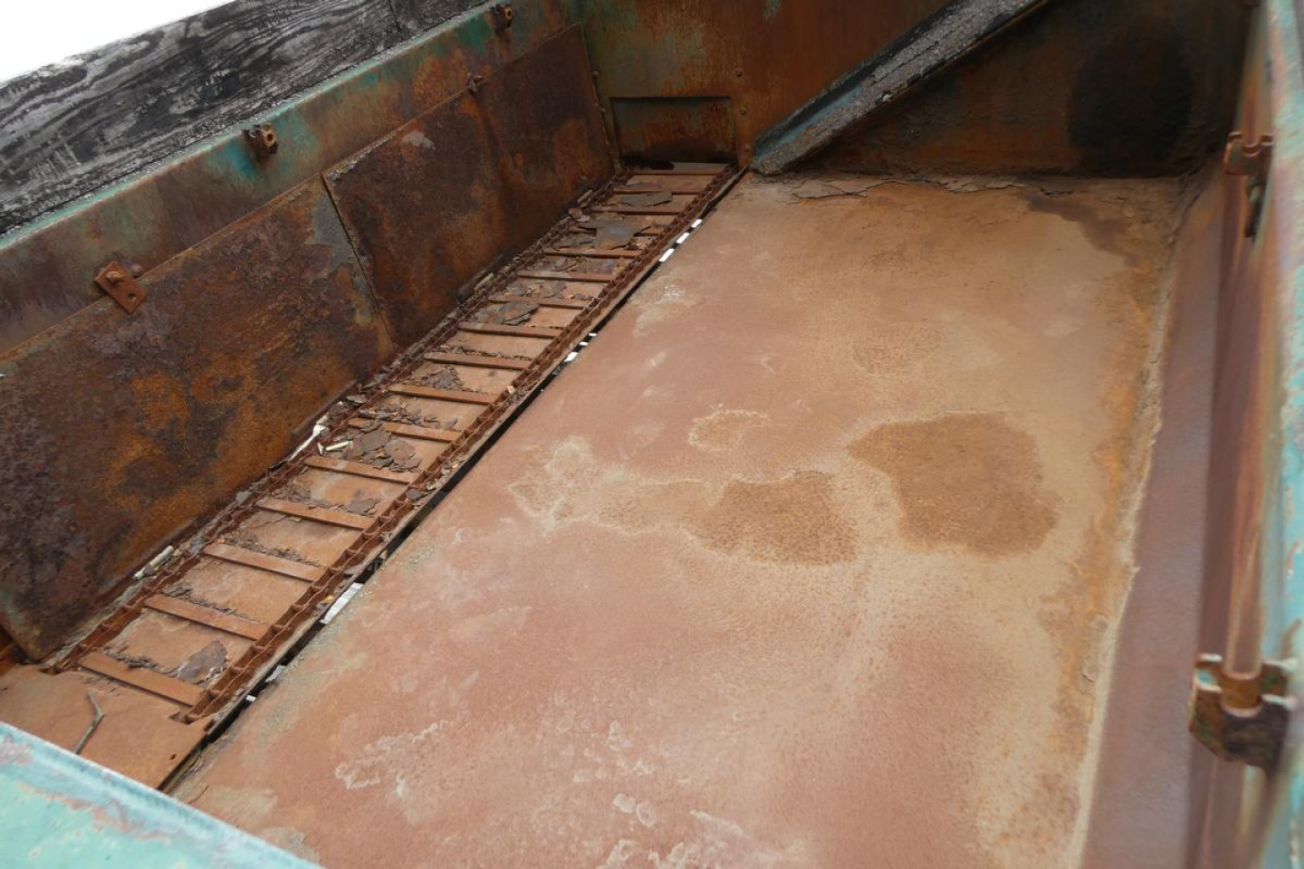 Dump truck bed interior showing rusty floor and sidewalls with metal racking along the left side.