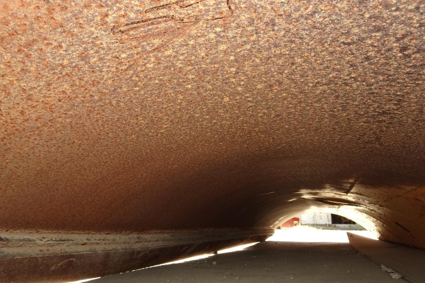 Dump truck undercarriage showing rust-colored interior of a dump bed tunnel.