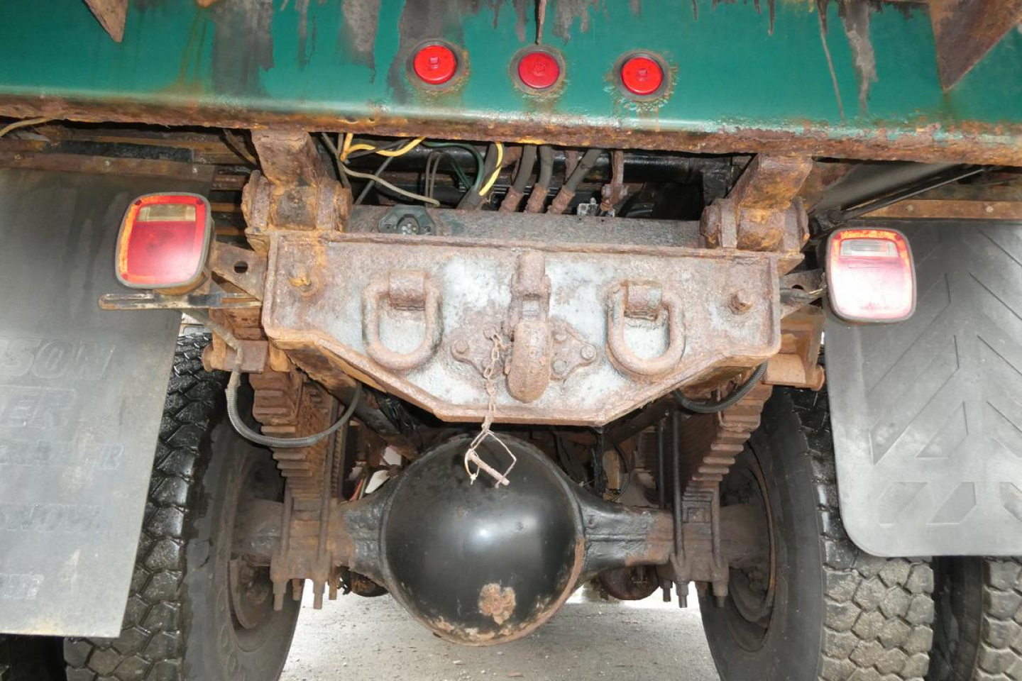Back view of Mack GU (Granite) GU712 chassis showing rear differential housing, suspension, and frame; two rectangular red rear lights; rusted hitch area.