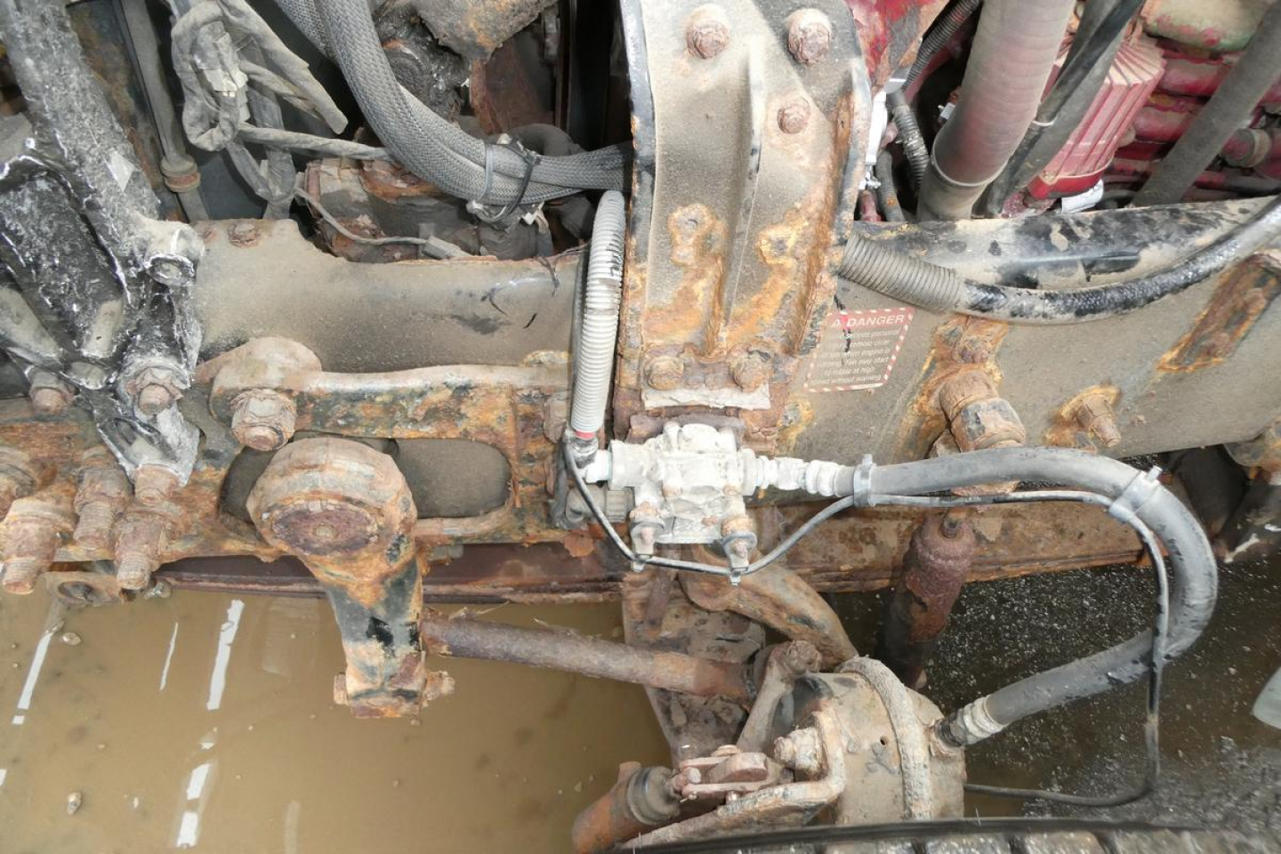 Mack GU Granite engine bay with hydraulic lines and steering linkage; rust and grime on frame and components.