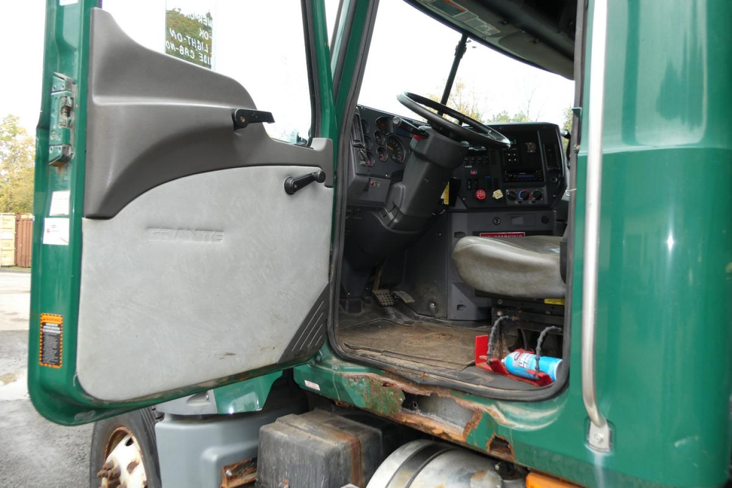 Truck cab interior and open door of a 2010 Mack GU granite series GU712 dump truck showing steering wheel dashboard and entry step.