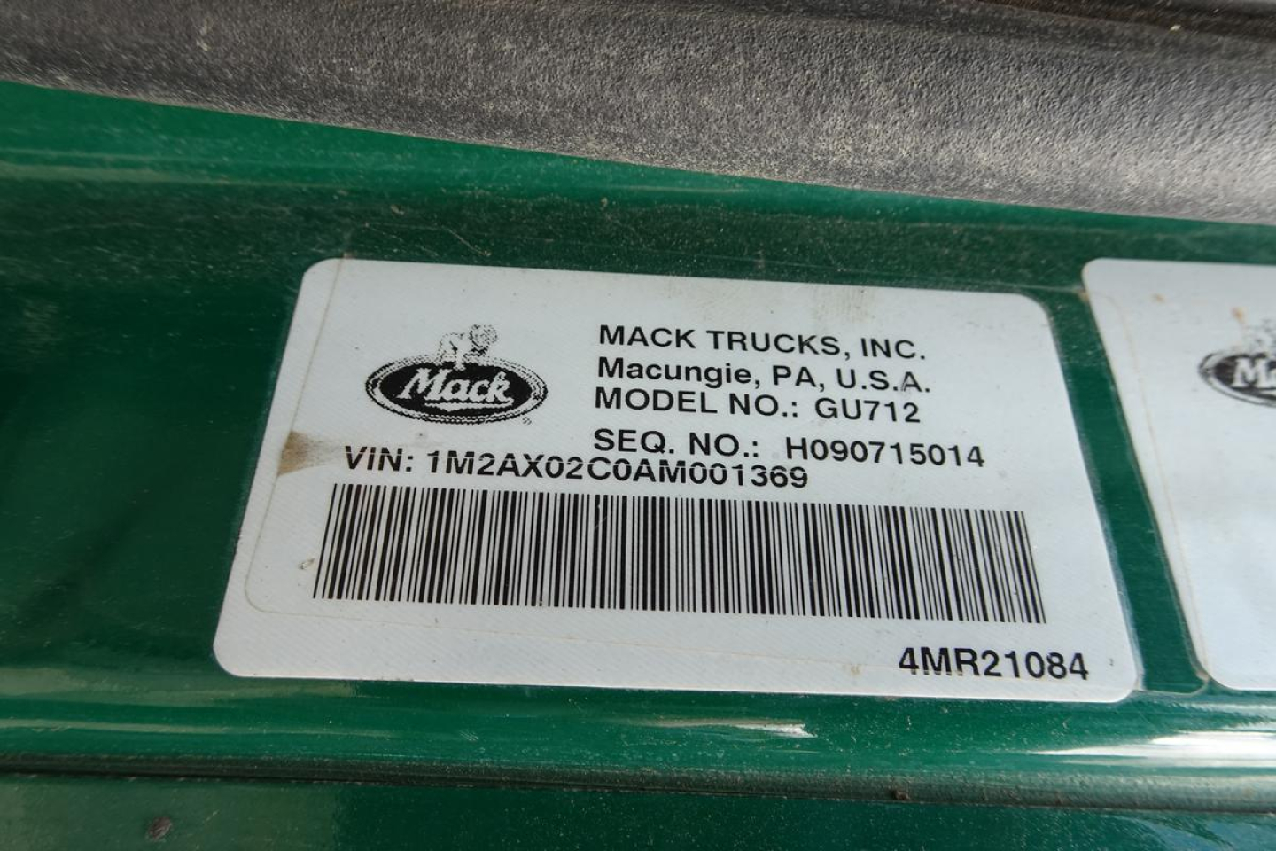 Mack Trucks label on dash area showing VIN: 1M2AX02CA ... unclear. Clear text includes MACK TRUCKS, INC., Macungie, PA, U.S.A., MODEL NO: GU712, SEQ. NO.: H09071501A, VIN: 1M2AX02C0AM001369, barcode, 4MR21084