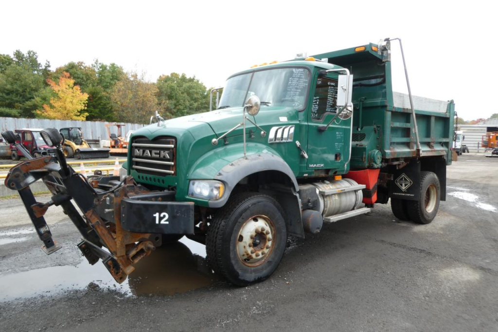 Mack GU Granite dump truck with front-mounted plow/digger attachment and green cab, showing side view, dump bed, large tires, and stock number 1009262.