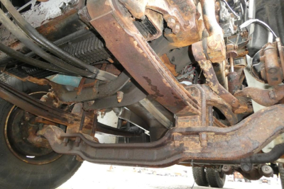Underbody view of a 2010 Mack GU (Granite) GU712 chassis showing rusted frame components and suspension parts.