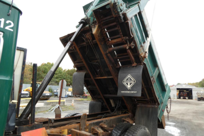Dump truck bed tilted for unloading showing hydraulic cylinder and underside with Mack Granite insignia and chassis.