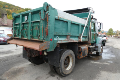 Dump truck rear and side view showing green Mack Granite GU712 dump bed, dual rear tires, rear hitch, and rusted chassis areas.