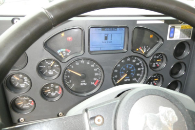 Dashboard of a Mack GU truck showing multiple gauges, digital display reading Low Fuel, speedometer up to 120, RPM gauge, and various indicator lights.