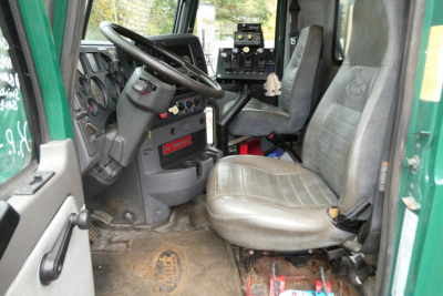 Cab interior of a Mack GU dump truck showing steering wheel, dashboard, and two seats with a worn floor mat.