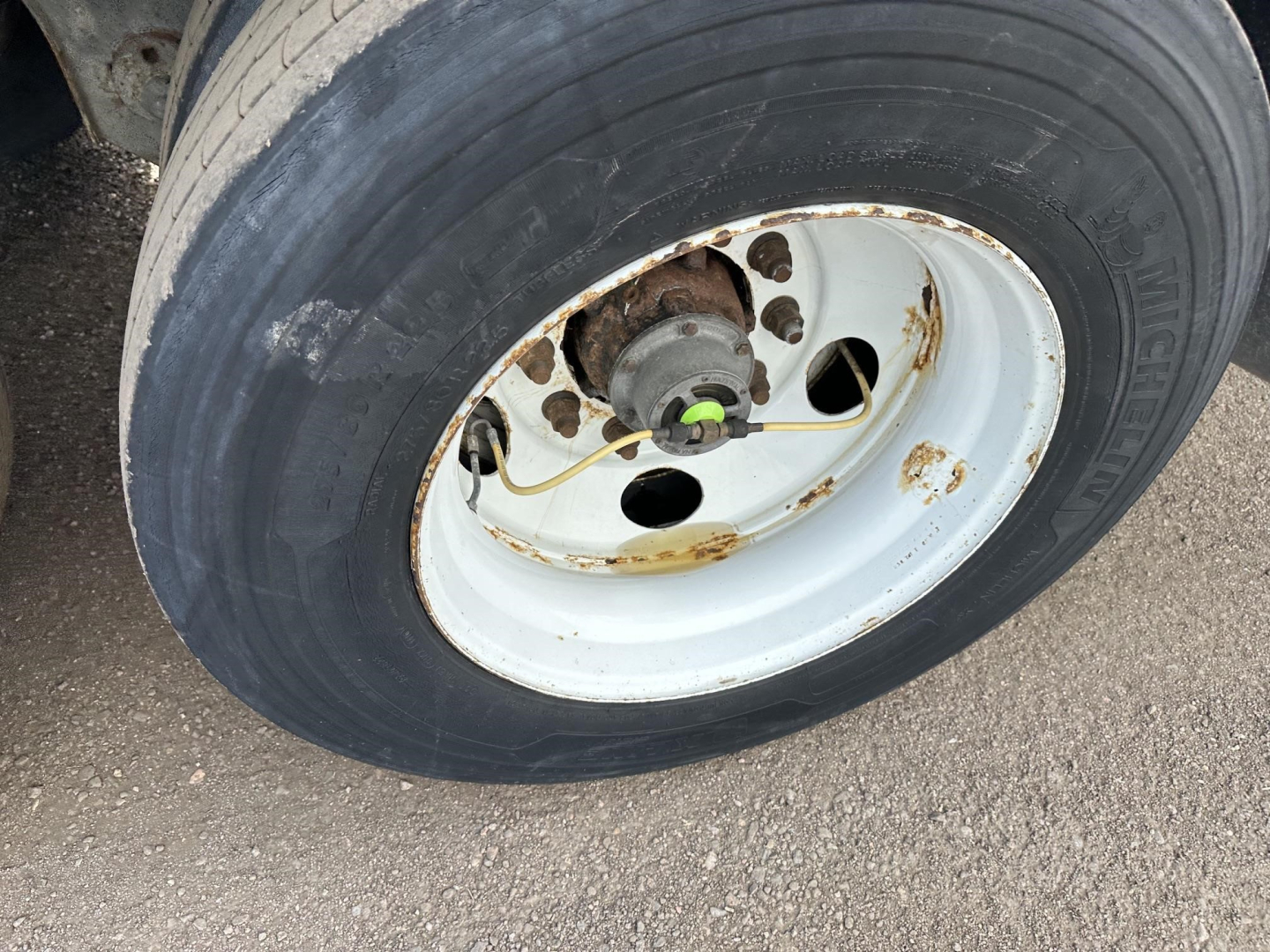 Trailer wheel and hub showing Michelin tire and white steel rim with rust spots and brake drum; green valve cap and rusted hub area.