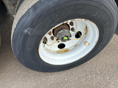 Trailer wheel and hub showing Michelin tire and white steel rim with rust spots and brake drum; green valve cap and rusted hub area.