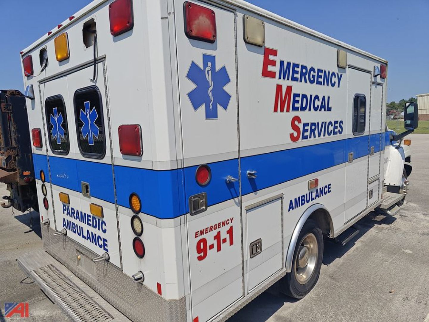 Ambulance side and rear showing Emergency Medical Services lettering and 9-1-1, paramedic ambulance text, blue stripe, rear doors, and medical star symbol.
