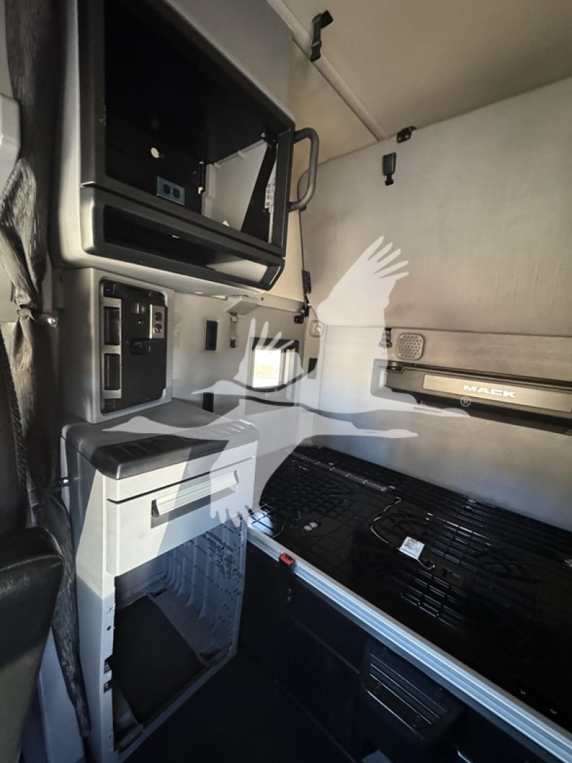 Truck cab interior showing dashboard area with storage compartments and a walk-through sleeper, light gray panels, black steps, and a large grill area visible.
