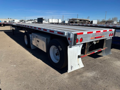 Flatbed trailer in side view showing aluminum deck and dual rear axles with reflective tape and mud flaps.