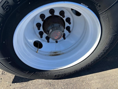 Flatbed trailer wheel with white steel rim and black tire showing lug nuts and hub, no legible brand text visible.