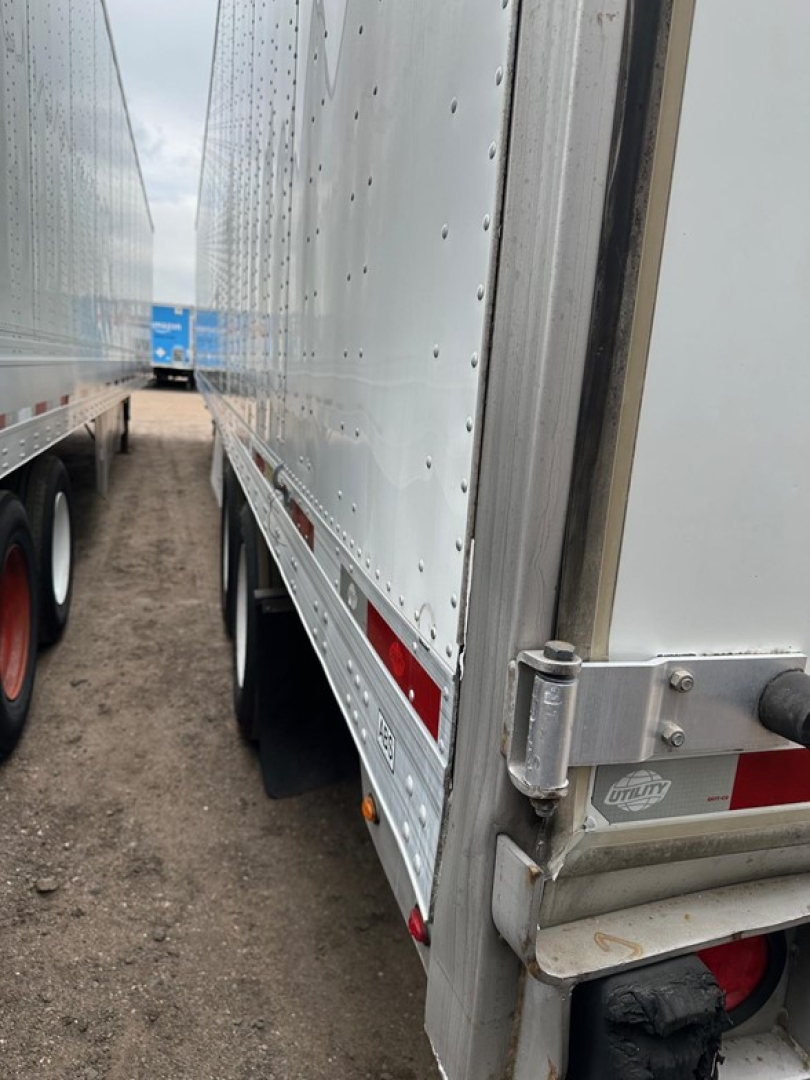 Trailer side of a used Utility 4000Dx semi-trailer showing riveted aluminum siding, rear latch, and reflective tape along the lower edge.