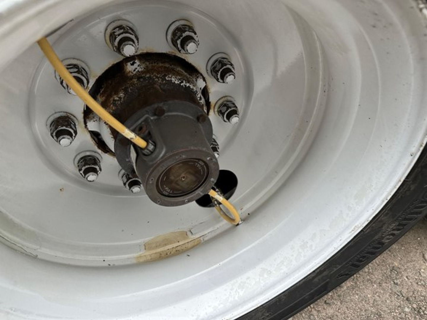 Trailer wheel hub with yellow cable, white rim, and lug nuts; close-up of axle hub area showing electrical plug on wheel.