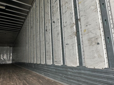 Trailer interior wall with vertical metal studs and ribbed floor showing worn aluminum panels and interior trailer space.