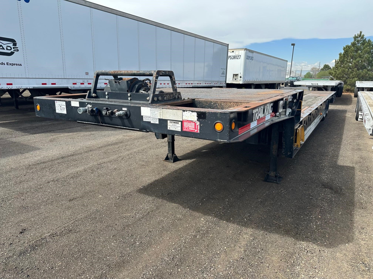 Trailer rear view showing 40-ton hydraulic tail with air ride and long flat deck, with ramps and hitch assembly visible.