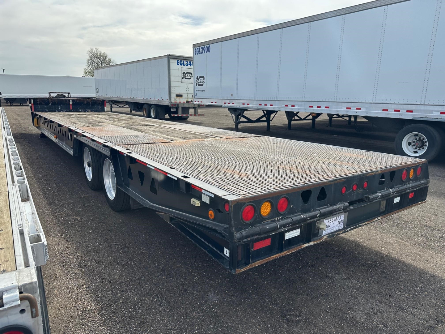 Flatbed trailer showing 40-ton hydraulic tail, steel deck, dual rear axle, and lighting on rear with taillights and reflectors.