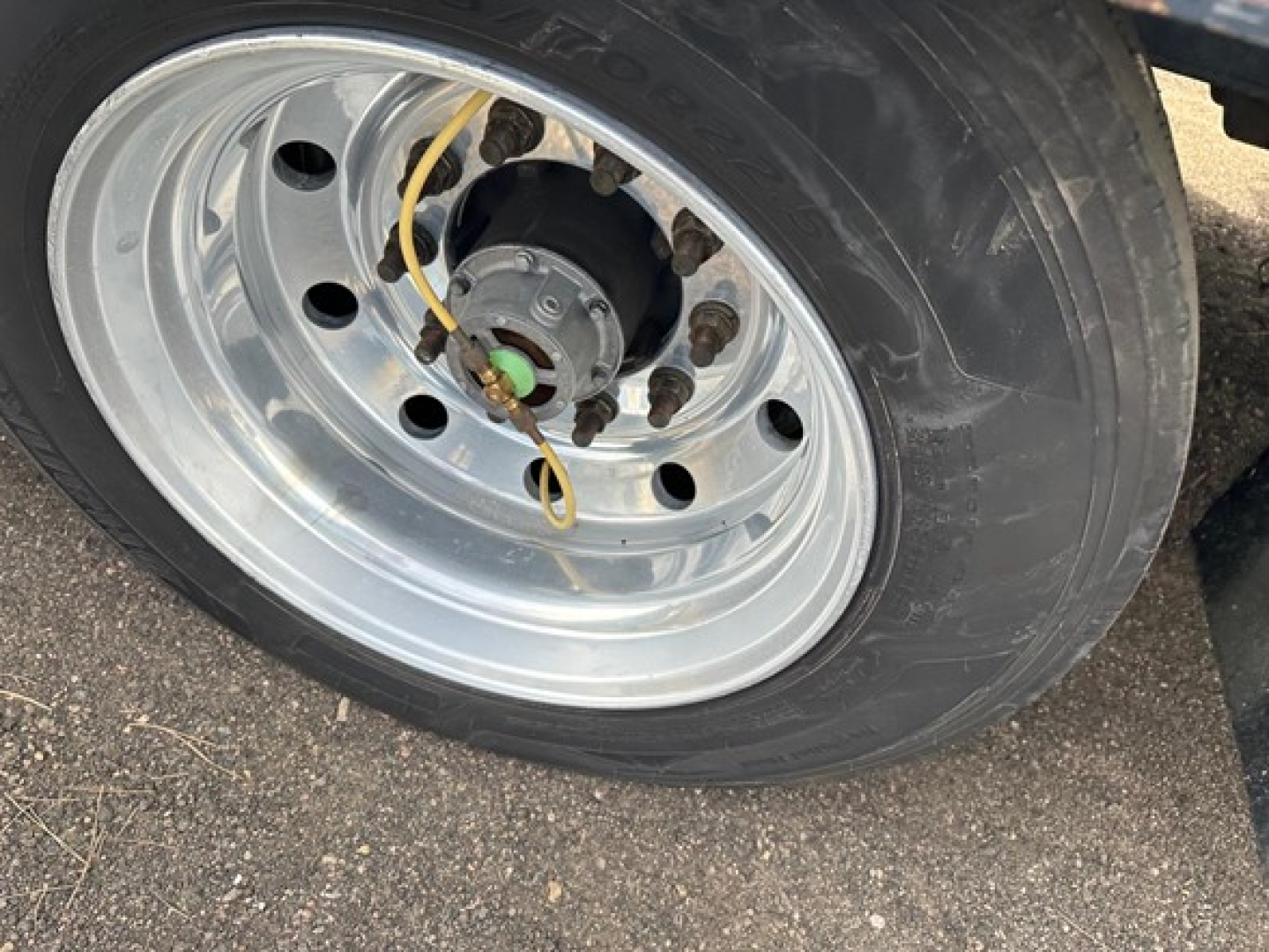Wheel of a Trail King 40 Ton hydraulic tail trailer showing a polished steel rim, tire, and hub with yellow line and green center cap.