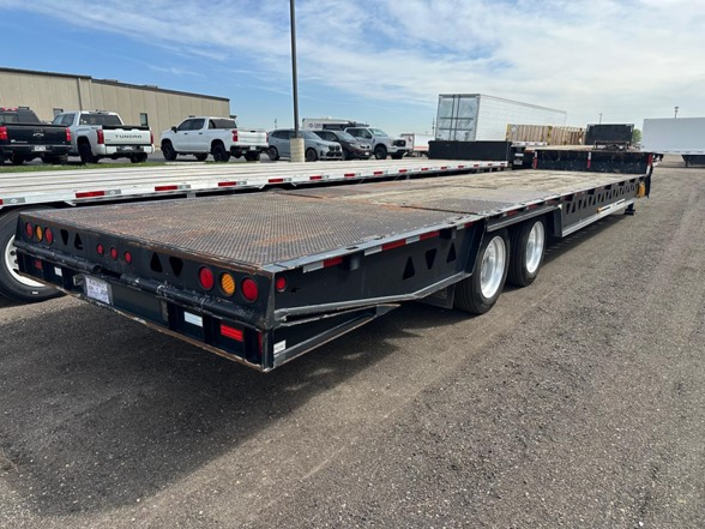 Trailer showing a long flatbed hydraulic tail 40 ton Trail King trailer with dual rear axles and steel deck.