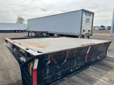 Flatbed trailer with a hydraulic tail and rust-streaked surface, 48' long, diamond plate deck, dirt and wear visible.