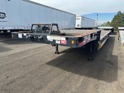 Trailer: 2017 Trail King 40 Ton hydraulic tail trailer in a parking lot, flatbed with deck; front hitch and support legs visible; other trailers in background.
