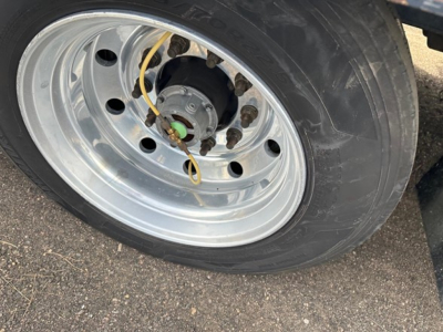 Wheel of a Trail King 40 Ton hydraulic tail trailer showing a polished steel rim, tire, and hub with yellow line and green center cap.