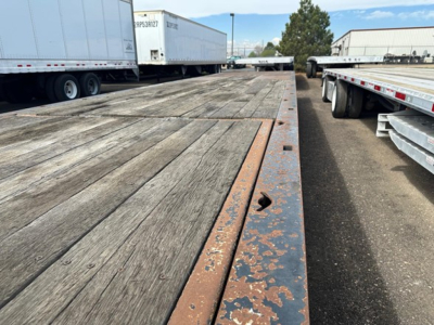 Trail King 40 ton hydraulic tail trailer deck view showing wooden planks and rusted steel edge on a gooseneck trailer, with other trailers in background.