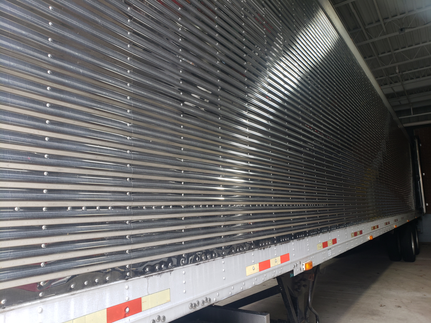 Great Dane 53' dry van trailer side view showing corrugated aluminum walls, side reflective tape, and undercarriage with wheel wells inside a warehouse.
