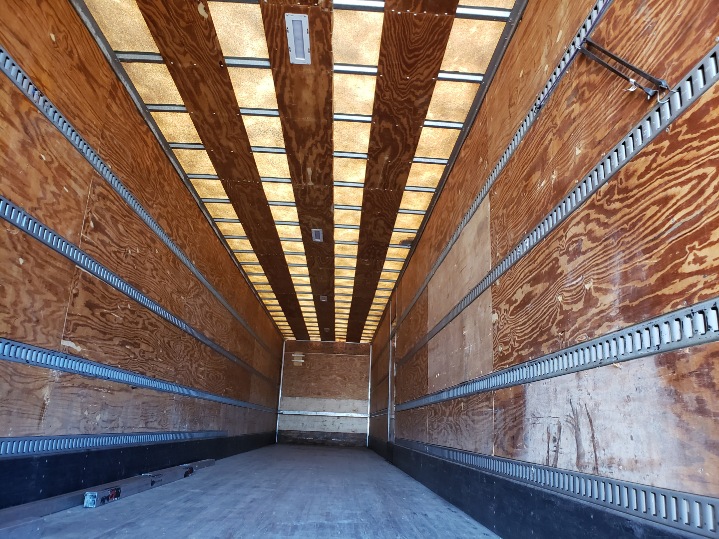Trailer interior showing wooden side walls and metal E-track rails in a 53' dry van with empty cargo area.
