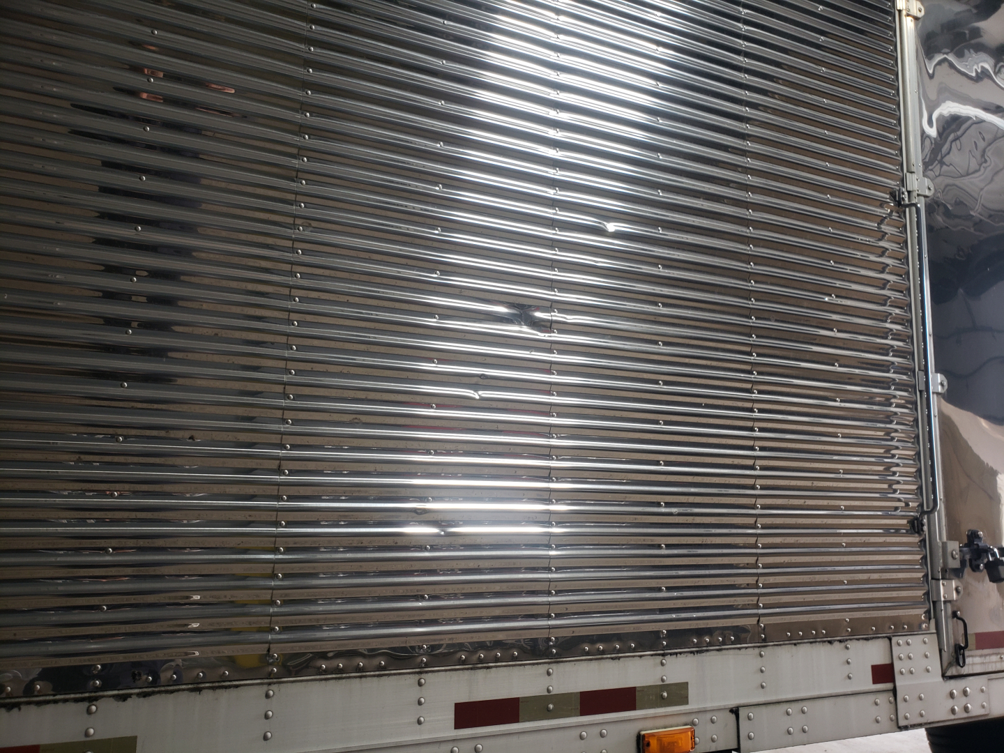 Trailer side showing corrugated aluminum cargo door with horizontal ribs, lower white panel with rivets and reflective tape.
