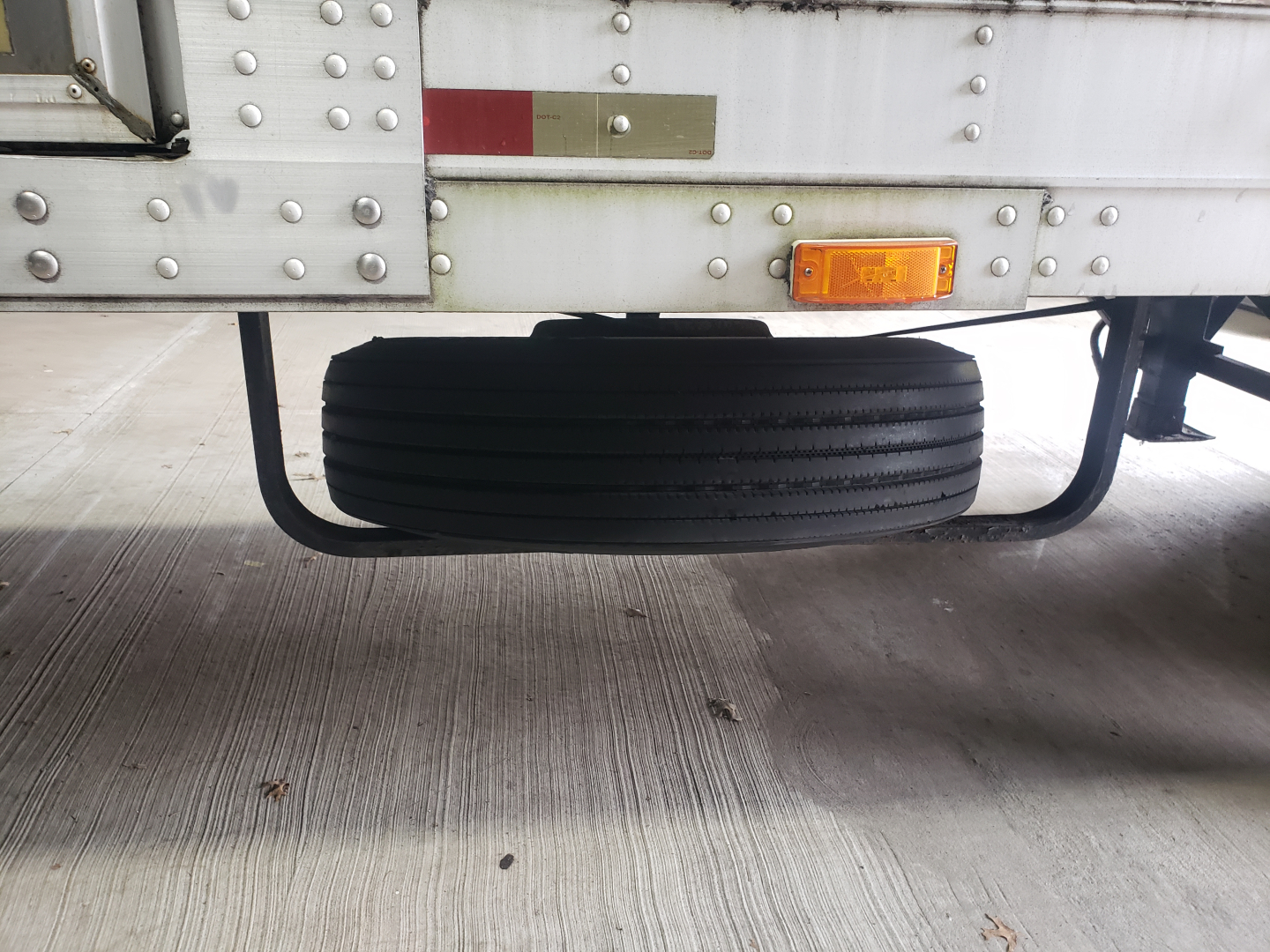 Trailer undercarriage showing spare or storage tire mounted on rear underside of a 53' Great Dane dry van trailer with riveted aluminum panels and an amber reflector.