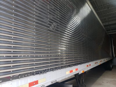 Great Dane 53' dry van trailer side view showing corrugated aluminum walls, side reflective tape, and undercarriage with wheel wells inside a warehouse.