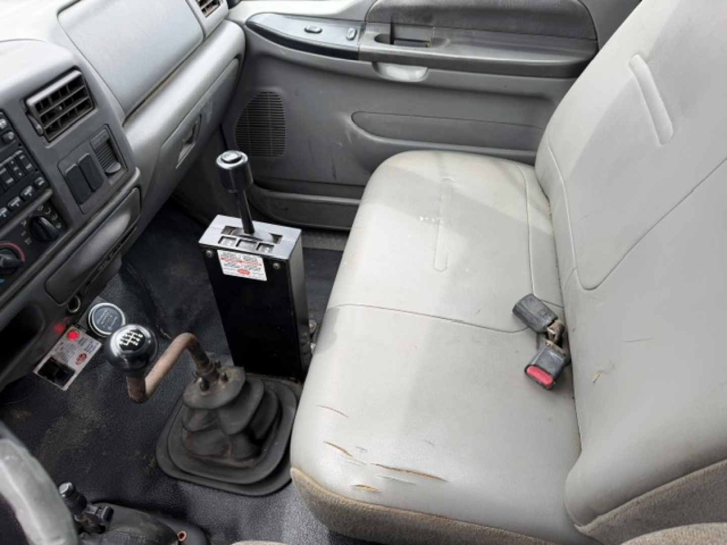 Cab interior of a 2006 Ford F750 SD dump truck showing manual shifter, center console, beige seat with wear, and gear stick with labels.