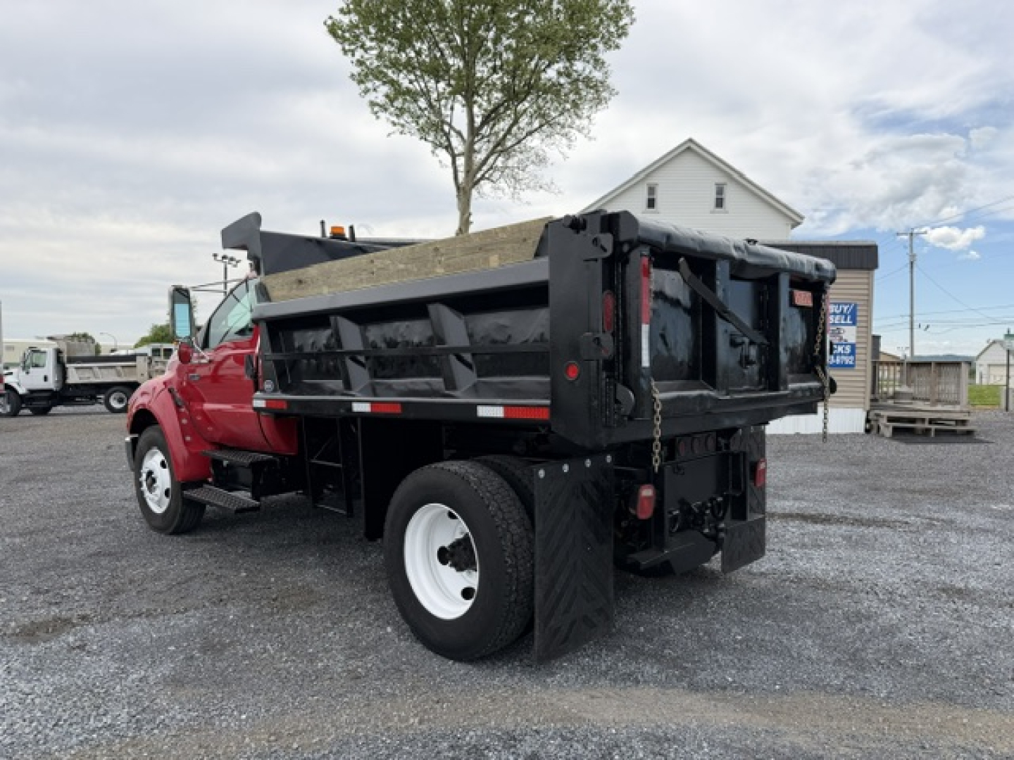 Dump truck with red cab and black dump bed in a lot, rear view showing lift mechanism and side mirrors.