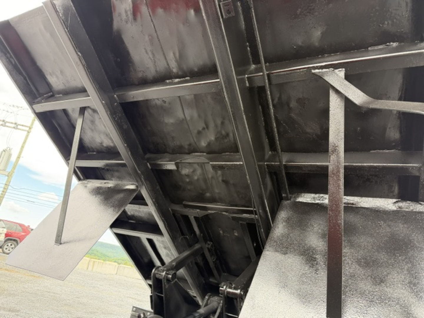 Dump truck bed underside showing hydraulic components and metal support beams.