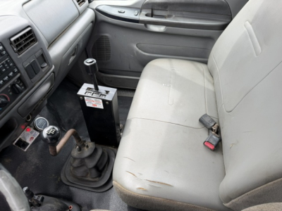 Cab interior of a 2006 Ford F750 SD dump truck showing manual shifter, center console, beige seat with wear, and gear stick with labels.