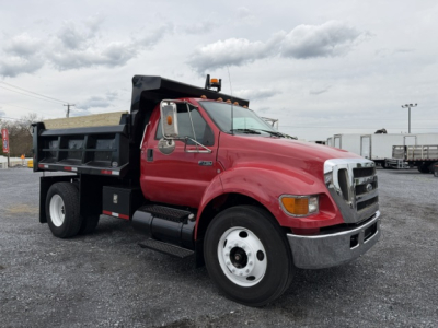 Truck side view showing red Ford F-750 SD dump truck with black dump bed, chrome bumper, and white wheels. Text on image includes VIN and stock number not visible on vehicle.