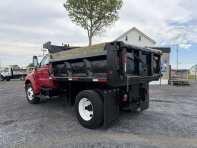 Dump truck with red cab and black dump bed in a lot, rear view showing lift mechanism and side mirrors.