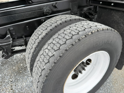 Truck wheel and dual rear axle area showing tire, white wheel rims, and chassis frame.