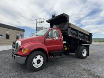 Ford F-750 SD dump truck showing red cab and black dump bed with stakes and hydraulic lift.