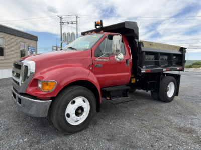 Red Ford F750 SD dump truck with black dump body, side view showing front grille and wheel.