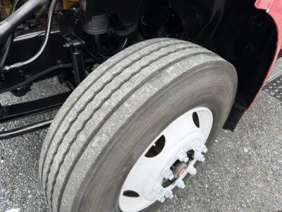 View of a front axle and tire on a 2006 Ford F750 SD dump truck showing dual rear? front wheel with white rim and tire treads; part of chassis and suspension visible.